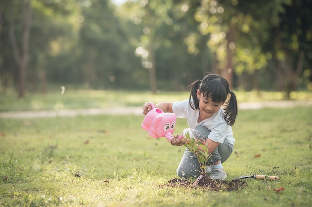 Menina criança asiática derramando água nas árvores. criança ajuda a cuidar das plantas com um regador no jardim.