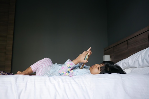 Menina criança assistindo desenho animado no telefone inteligente deitada na cama