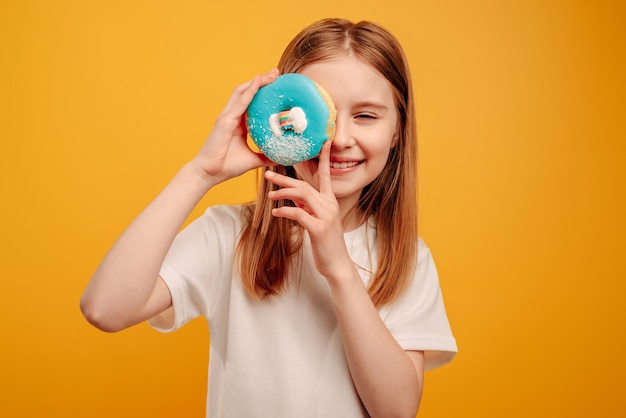 Menina criança com doce donut azul sniling isolado em fundo amarelo com copyspace retrato de be ...