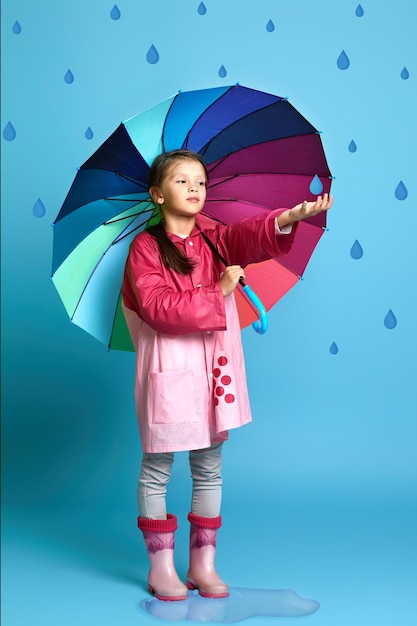 Menina criança com guarda-chuva multicolorido em capa de chuva rosa