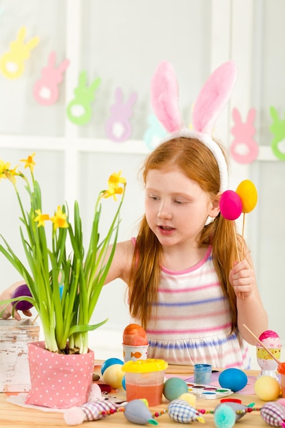 Menina criança com orelhas de coelhinho da Páscoa pintando ovos de Páscoa