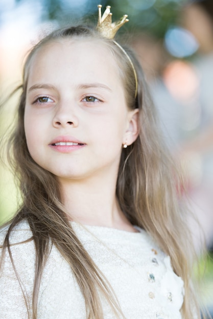 Menina criança com rosto calmo com minúscula coroa dourada na cabeça natureza fundo desfocado Menina princesa