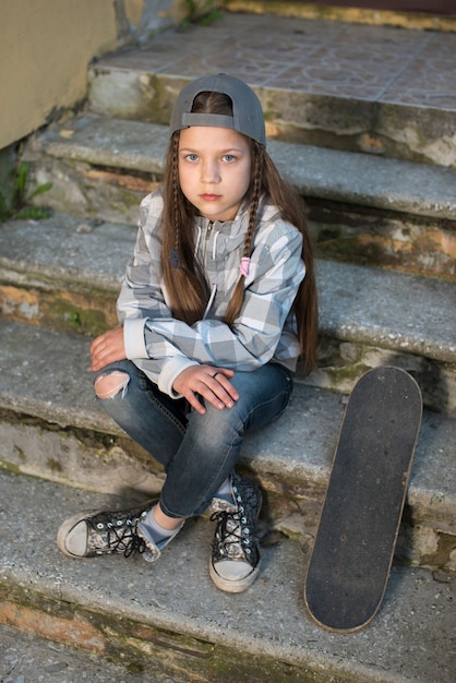 Menina criança com skate sentada na escada de concreto