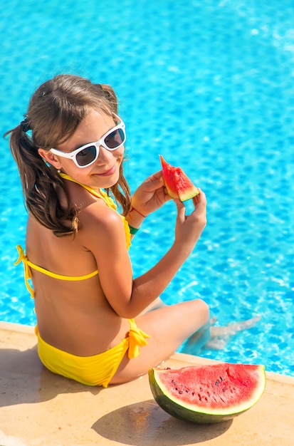 Menina criança comendo melancia perto da piscina