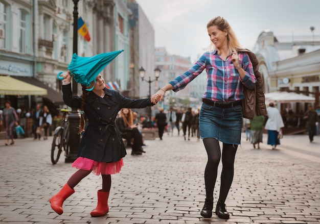 Menina criança de 6 anos de idade com um guarda-chuva em botas de borracha, se divertindo com a mãe em um banco no centro de Moscou no outono ou primavera.