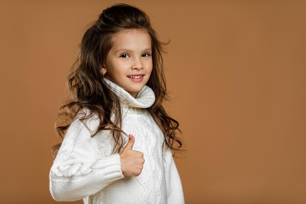 Menina criança de suéter branco, mostrando os polegares