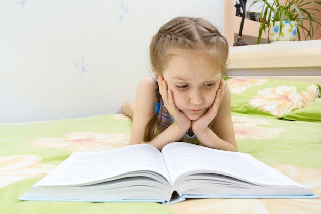 Menina criança deitada em uma cama e lendo um livro