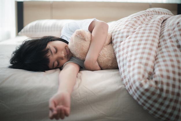 Menina criança dormindo na cama com um ursinho de pelúcia