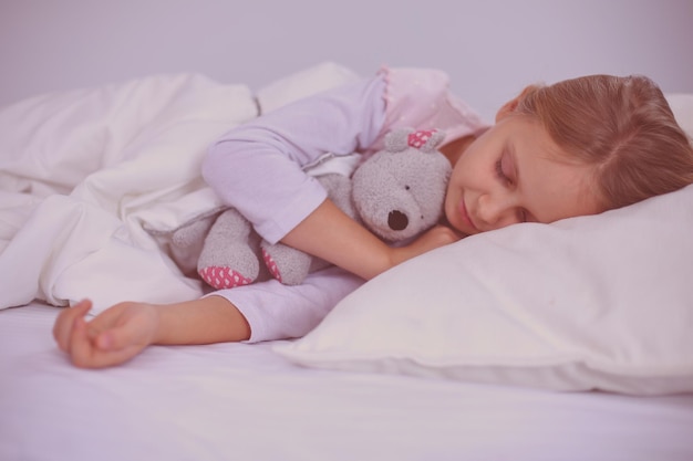 Menina criança dormindo na cama com um ursinho de pelúcia