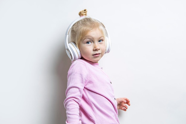 Menina criança em fones de ouvido ouve música em um fundo claro.