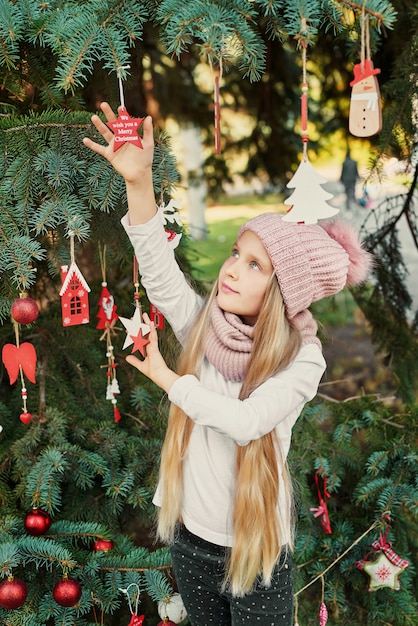 menina criança em um chapéu e lenço perto da árvore de Natal