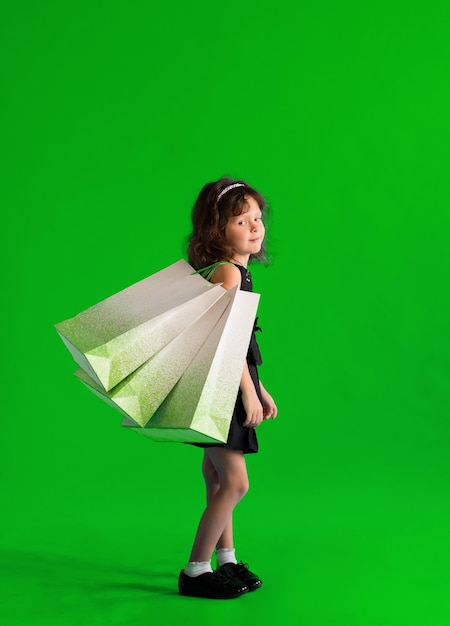 Menina criança em um vestido preto com sacos de papel em um fundo liso. Loja de descontos