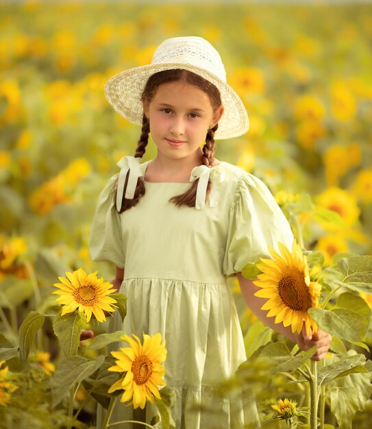 menina criança em um vestido verde e chapéu branco fica em um campo com girassóis