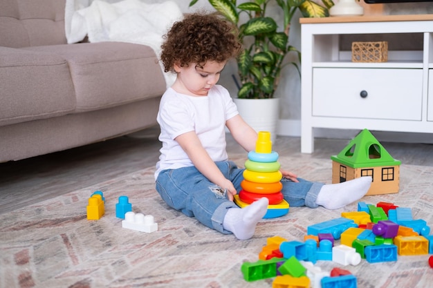 Menina criança encaracolada brincando com pirâmide e construtor em casa desenvolvimento infantil