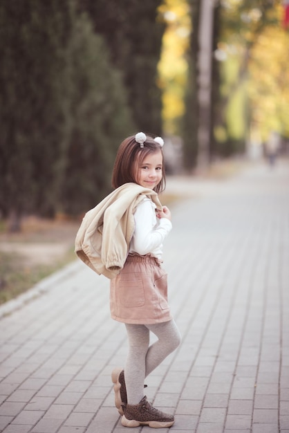 Menina criança estilosa segurando uma jaqueta e caminhando na rua ao ar livre