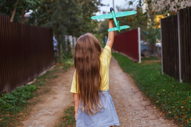 Menina criança feliz com longos cabelos loiros brincando com avião de brinquedo ao ar livre ao pôr do sol