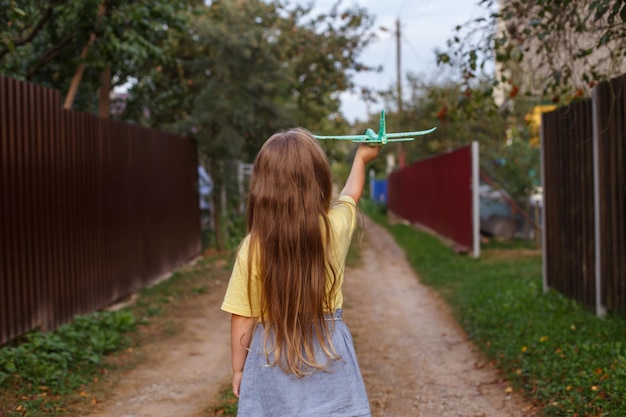 Menina criança feliz com longos cabelos loiros brincando com avião de brinquedo ao ar livre ao pôr do sol