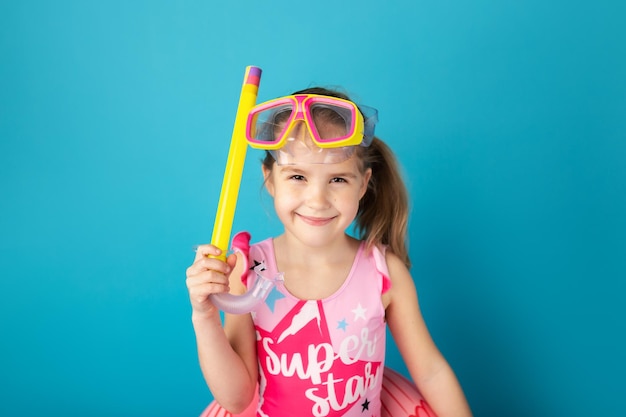 Menina criança feliz com máscara de natação e snorkel sorrindo e em pé acima do fundo azul