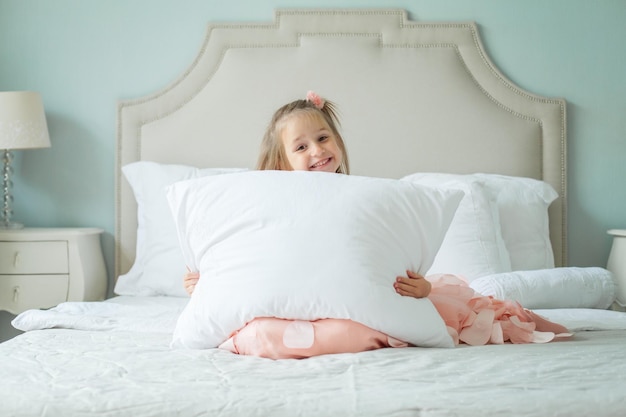 Menina criança feliz com travesseiro branco em casa