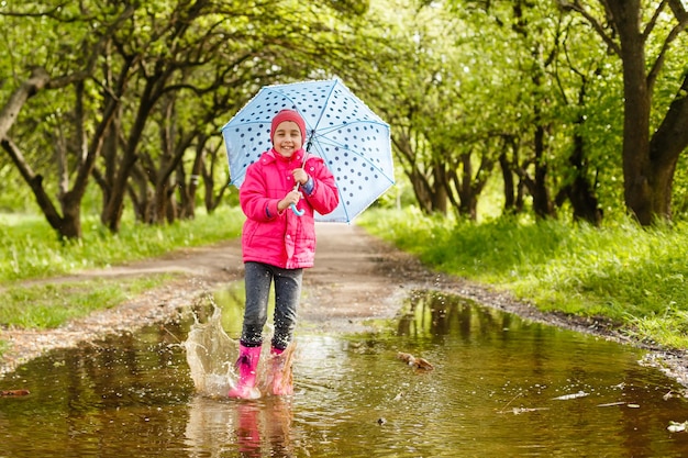 menina criança feliz com um guarda-chuva e botas de borracha em uma poça em uma caminhada de outono