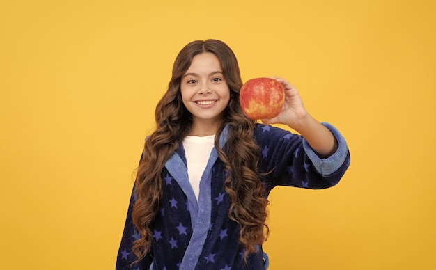 Menina criança feliz desfruta do café da manhã de maçã fresca em comida orgânica de roupão aconchegante