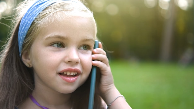 Menina criança feliz falando no celular no parque de verão.