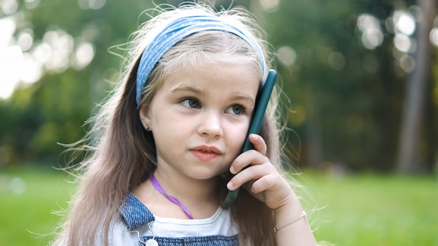 Menina criança feliz falando no celular no parque de verão.