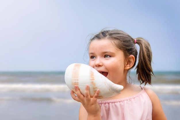Menina criança feliz gritando em uma concha na praia