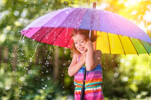 Menina criança feliz ri e brinca sob chuva de verão com um guarda-chuva