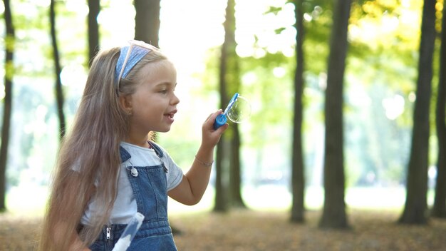 Menina criança feliz soprando bolhas de sabão ao ar livre no parque de verão.