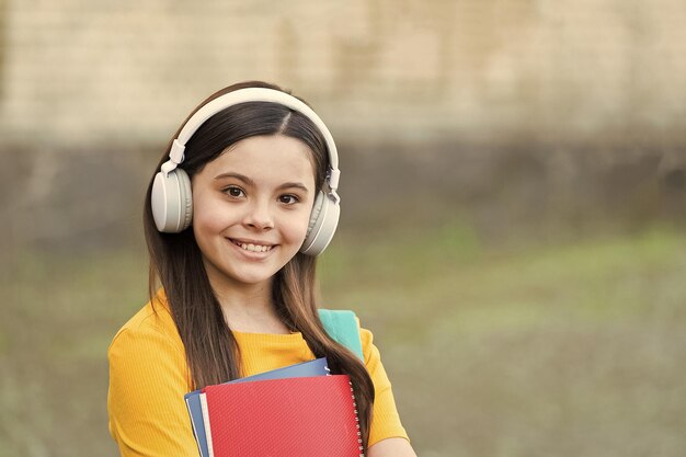 Foto menina criança moderna com fones de ouvido de volta à escola segura o conceito de abordagem moderna do livro didático