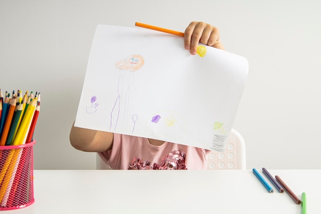 Menina criança mostra um desenho desenhado em papel enquanto está sentado à mesa