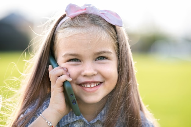 Menina criança muito feliz falando no celular, sorrindo ao ar livre no verão.