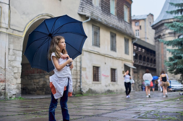 Menina criança na chuva com um guarda-chuva, fundo de cidade velha de turismo