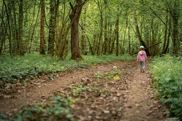 Menina criança na floresta densa caminha ao longo da trilha na floresta de profundidades.