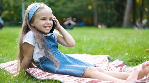 menina criança positiva conversando em seu telefone móvel no parque de verão.