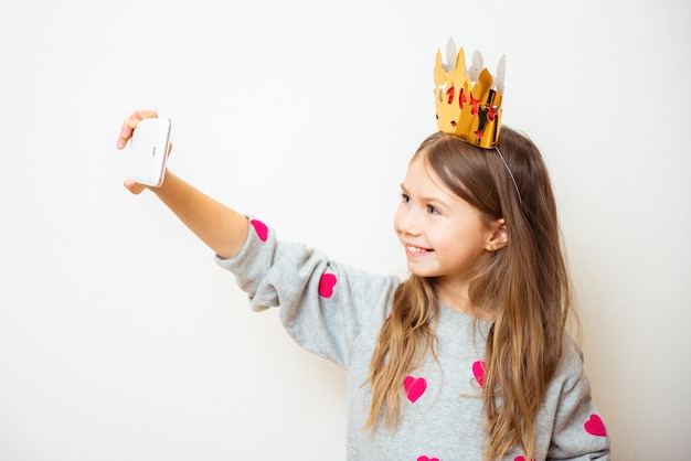 Menina criança positiva tira uma selfie com uma coroa na cabeça