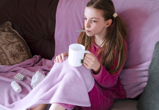 Foto menina criança, sentar cama, com, termômetro boca, cobertor, e, bebendo, chá