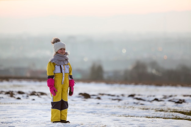 Menina criança sozinha ao ar livre no campo de inverno coberto de neve.