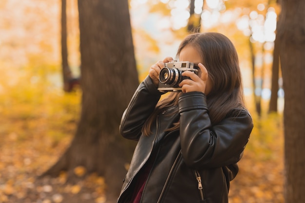 Menina criança usando uma câmera antiquada na natureza outono. Fotógrafo, temporada de outono e conceito de lazer.