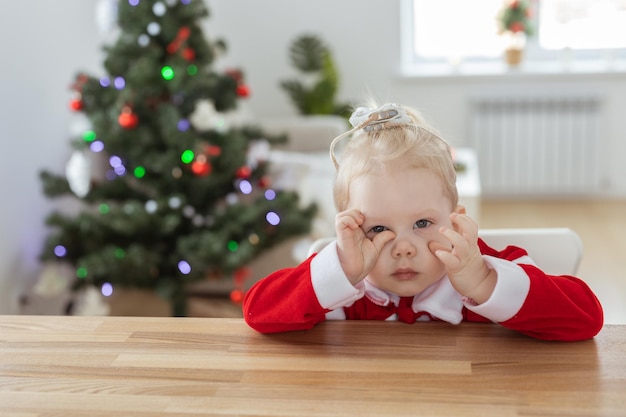 Menina criança vestida com vestido de natal com implantes cocleares se divertindo em casa com fundo de árvore de natal e aparelho auditivo de espaço de cópia e tecnologias inovadoras para tratamento de surdez