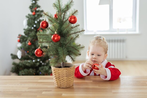 Menina criança vestida com vestido de natal com implantes cocleares se divertindo em casa com fundo de árvore de natal e aparelho auditivo de espaço de cópia e tecnologias inovadoras para tratamento de surdez