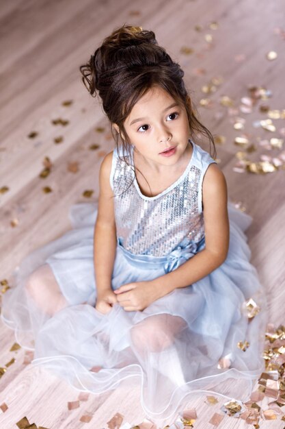 Menina criança vestida de azul, sentada no chão com confetes no fundo com bokeh prata. festa de aniversário