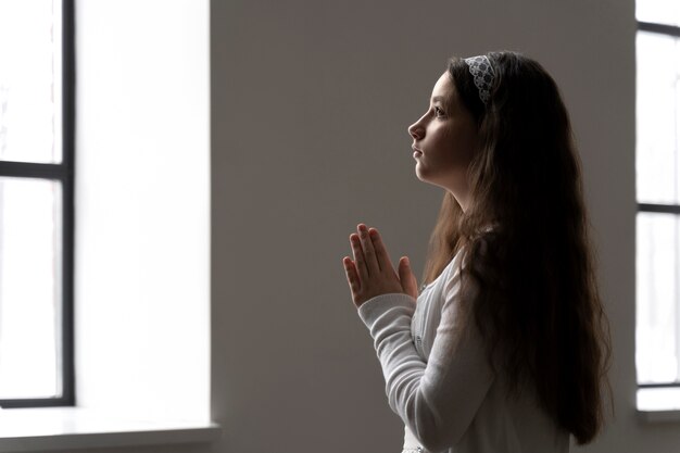Menina cristã de tiro médio rezando dentro