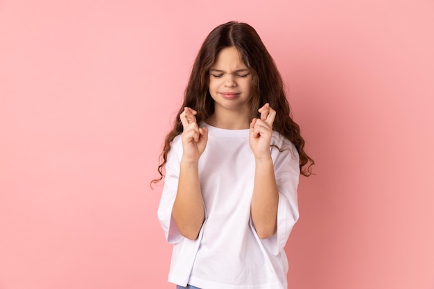 Menina cruzando os dedos na esperança de boa sorte fazendo rituais de desejo em pé com os olhos fechados