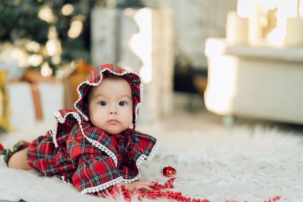 Menina curiosa de vestido vermelho brincando com brinquedos perto da árvore de Natal e presentes