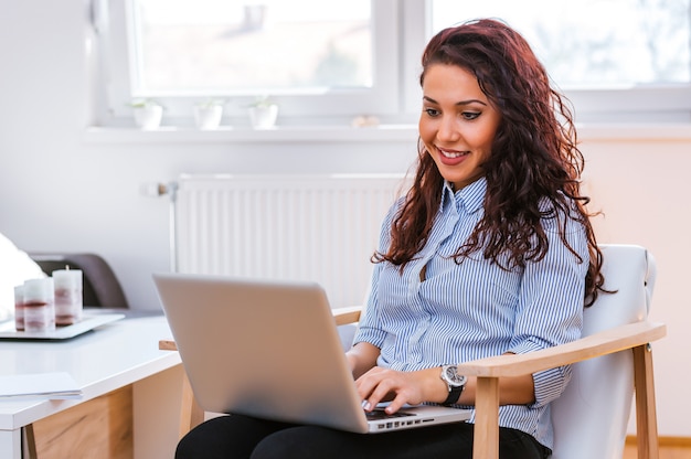 Menina curly usando seu lap top enquanto está sentado em uma cadeira