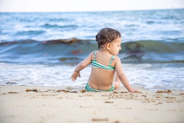 menina da criança sentada na praia e olhando para as ondas. vista traseira.