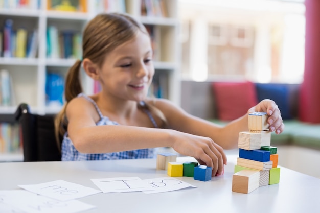 Menina da escola a brincar com bloco de construção na biblioteca a sorrir