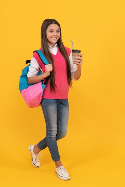 Menina da escola adolescente feliz com mochila bebida cacau para viagem em fundo amarelo, almoço.